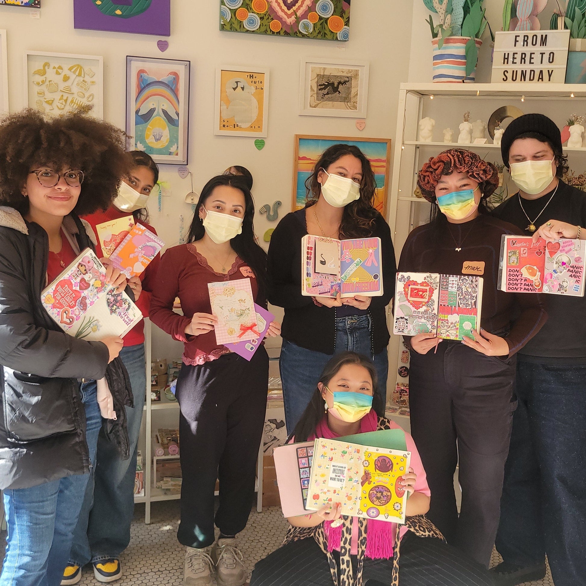 Group of people holding journals in a room with shelves and artwork.