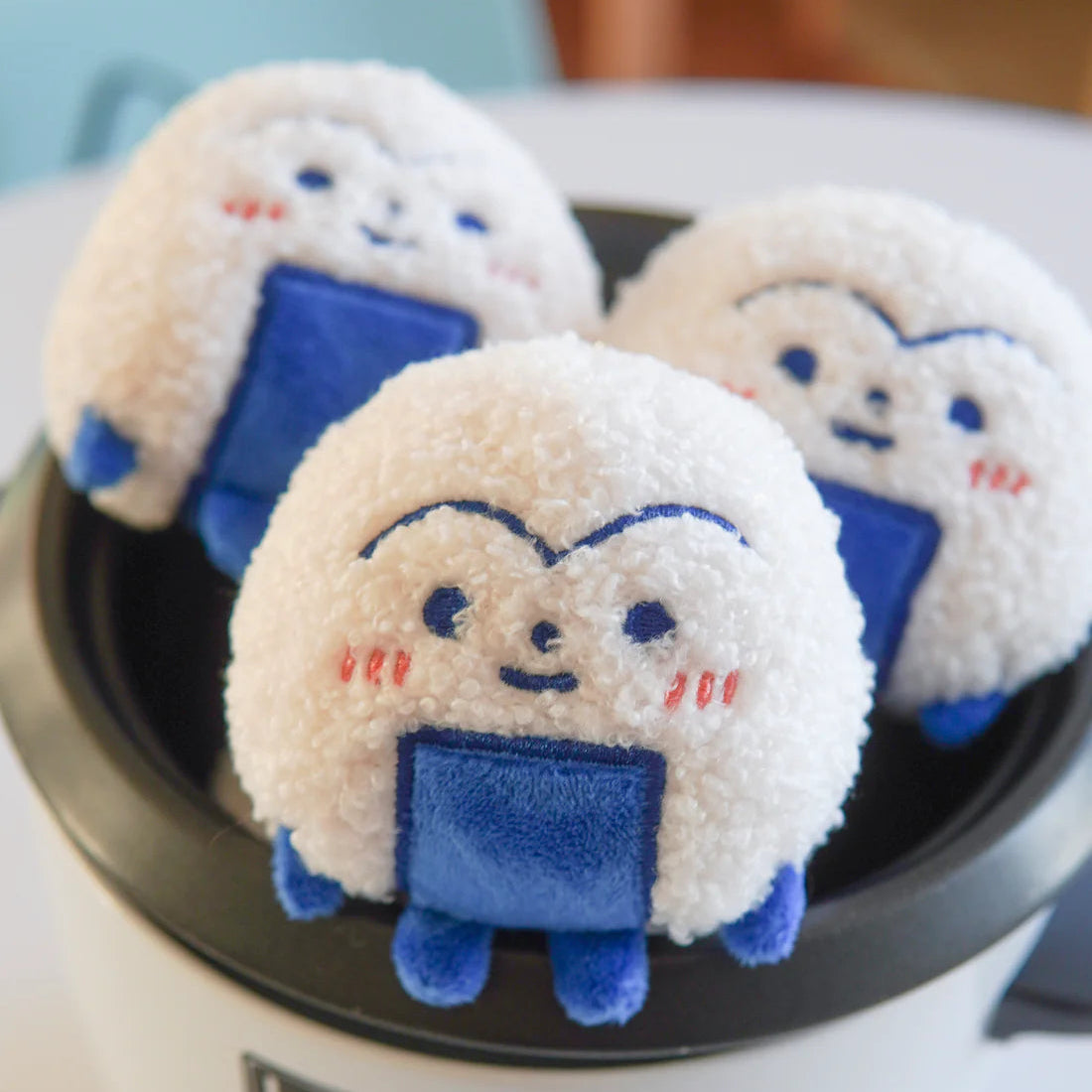 Three plush toys resembling cartoon characters with blue bodies and white faces on a white appliance.