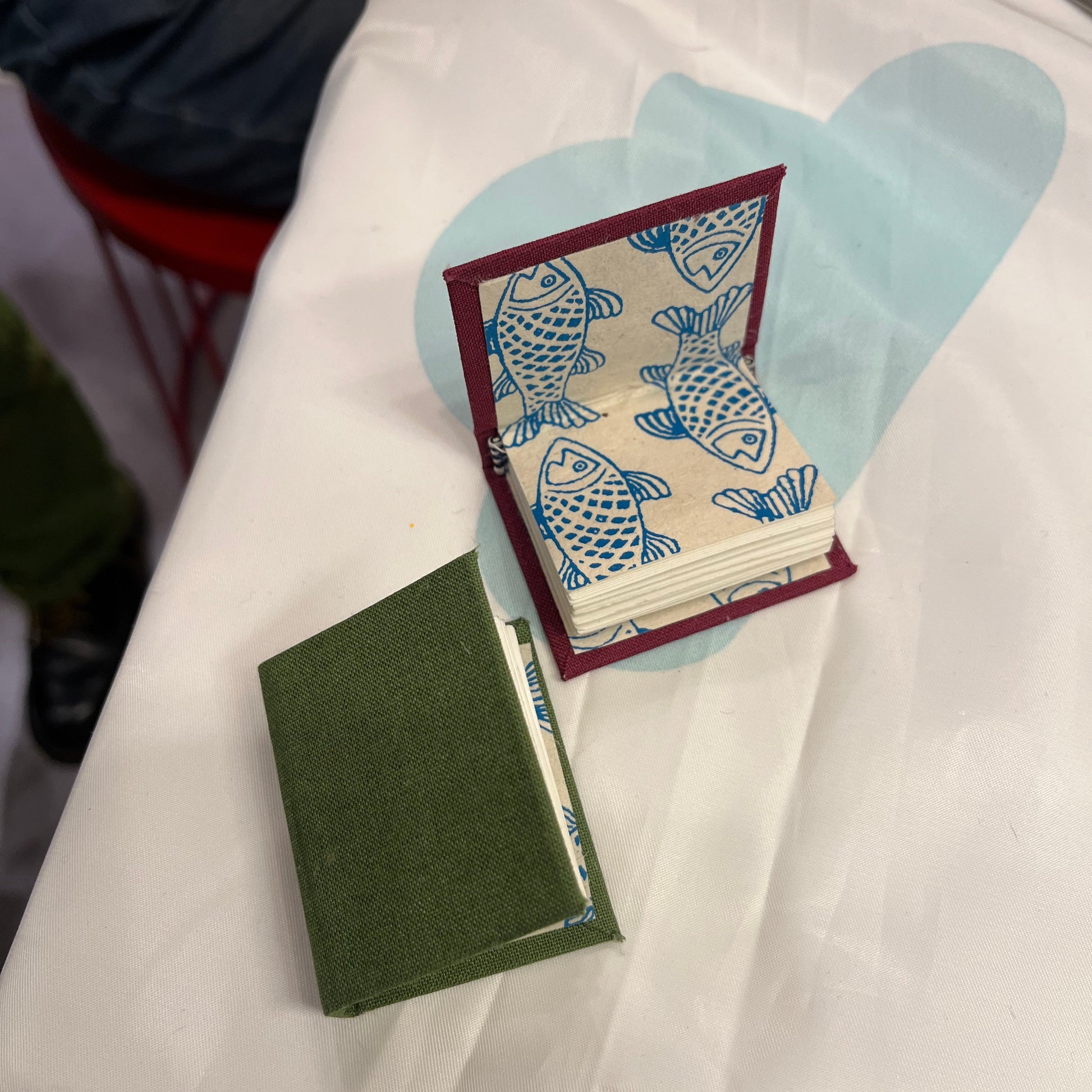 Two tiny handmade books with fish illustrations on a white surface